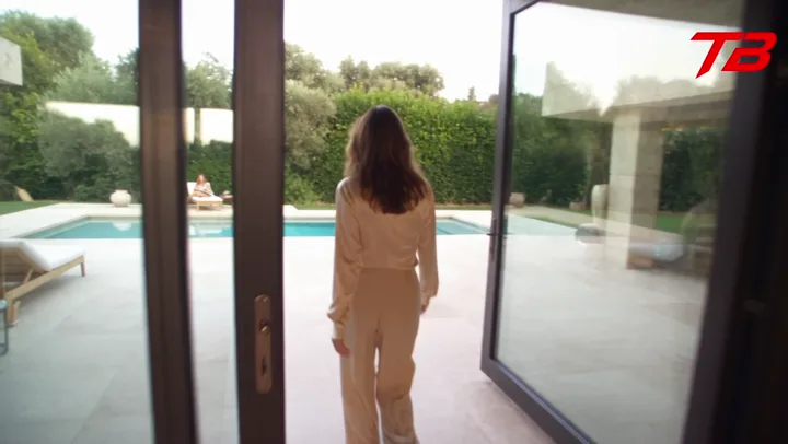 Mujer con ropa clara saliendo por un ventanal hacia la piscina de una villa de lujo.